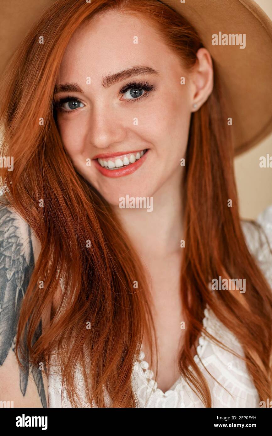 Happy redhead female with long hair and in stylish hat smiling and