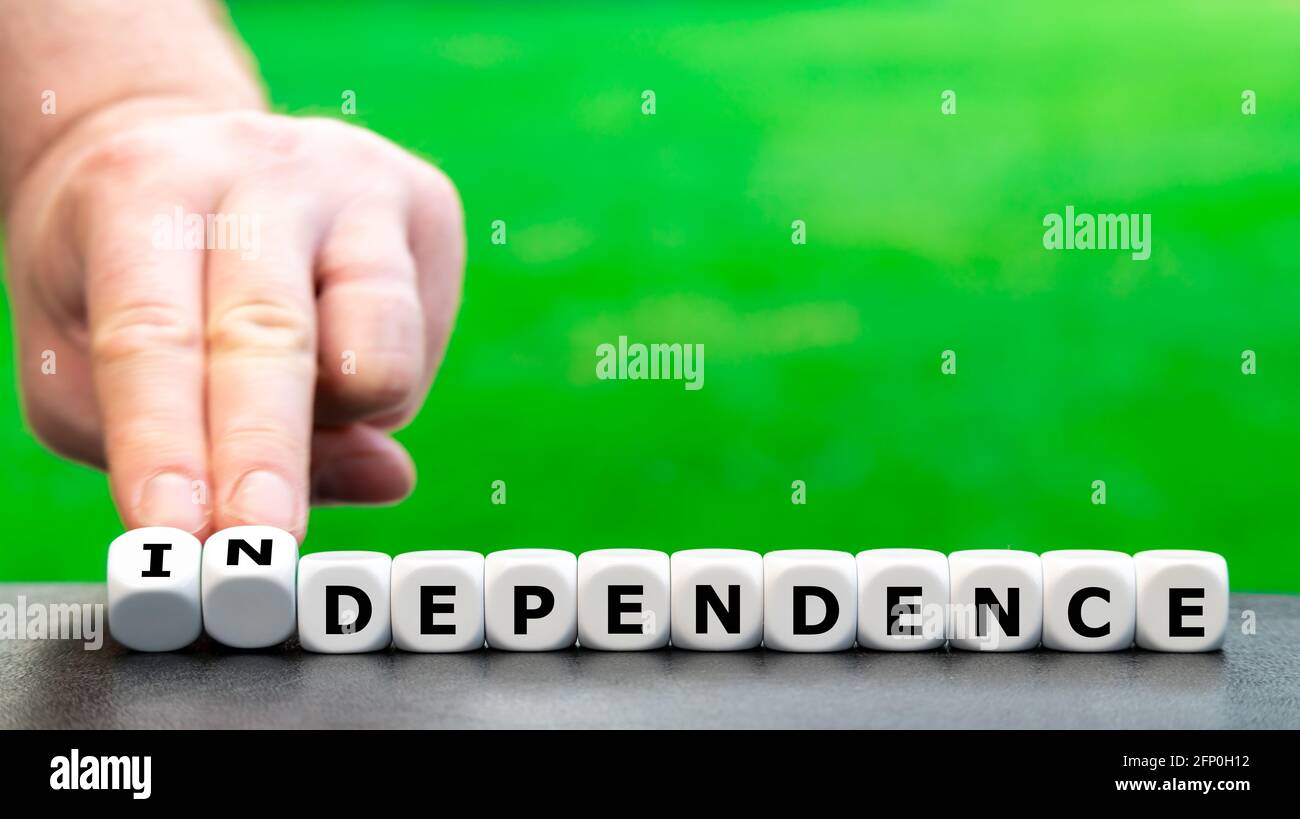 Hand turns dice and changes the word "dependence" to "independence". Stock Photo