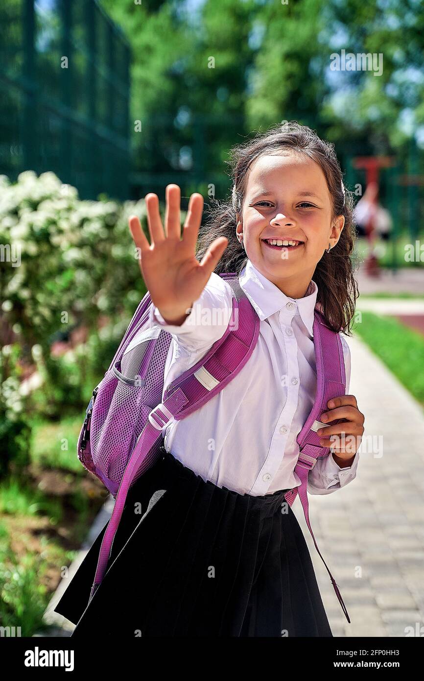 a schoolgirl girl in a white shirt with a backpack at school shows her