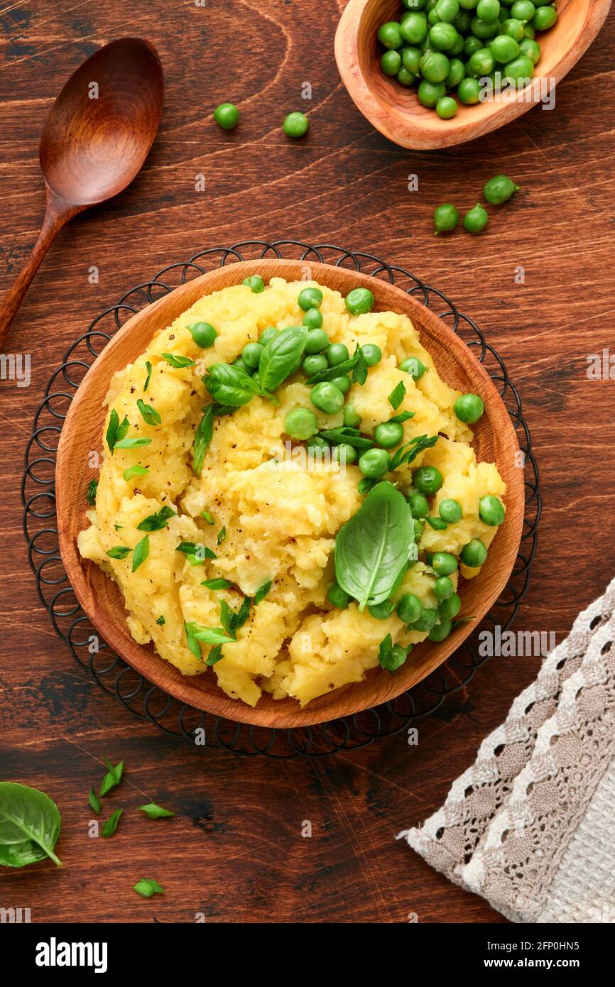 Mashed potato with butter, green peas, onions, basil on a rustic wooden background. Top view with close up. Stock Photo