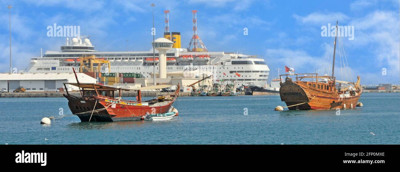 Muscat Dhows moored in Muttrah harbour in seascape with Costa cruise ship docked in Port Sultan Qaboos dock cranes & control tower Oman Gulf of Oman Stock Photo