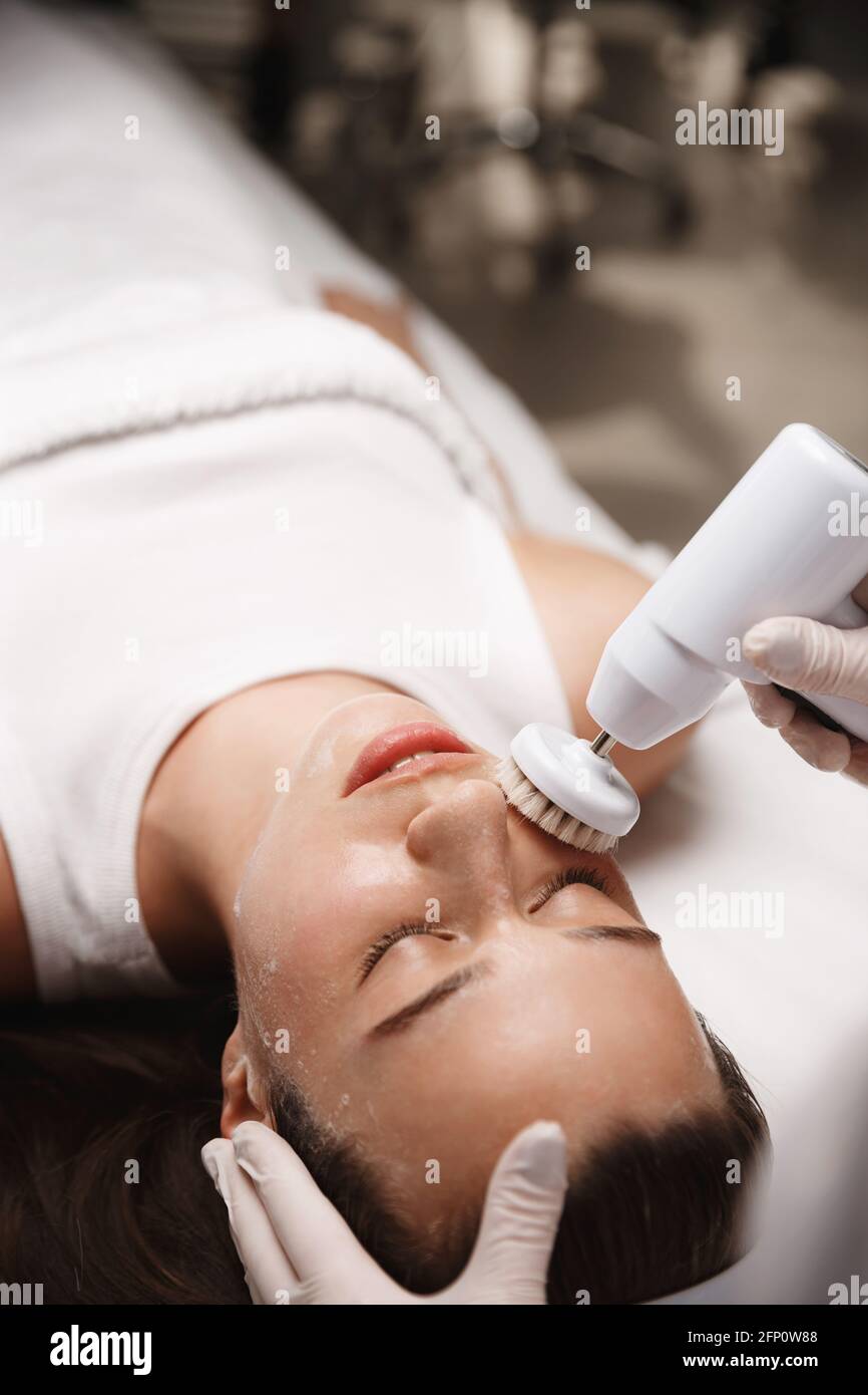 Hardware cosmetology and beauty salon. Face of young woman lying at beautician clinic, doctor using cleansing deep scrubbing rotating brush with Stock Photo