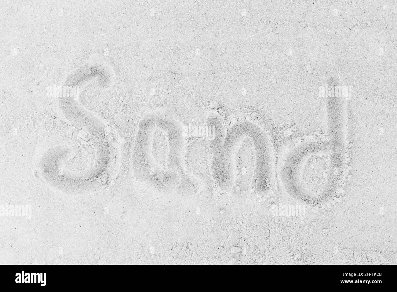 The word sand is written on a white beach sand background. Sign or symbol of sand concept. Stock Photo