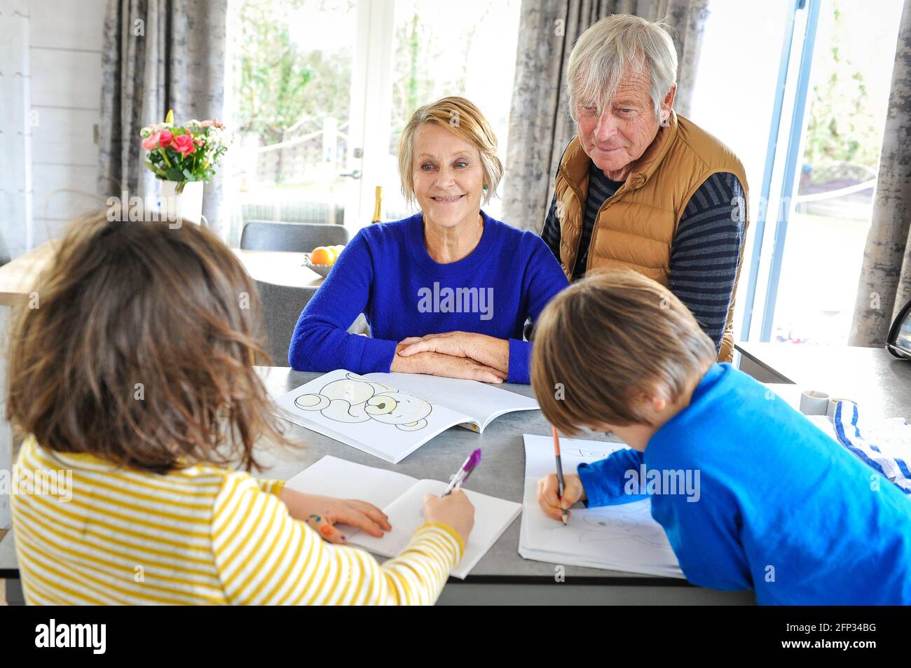 A retired couple spending time with their grandchildren on a holiday in Cornwall UK. Entertaining the grandchildren drawing and colouring pictures. Stock Photo