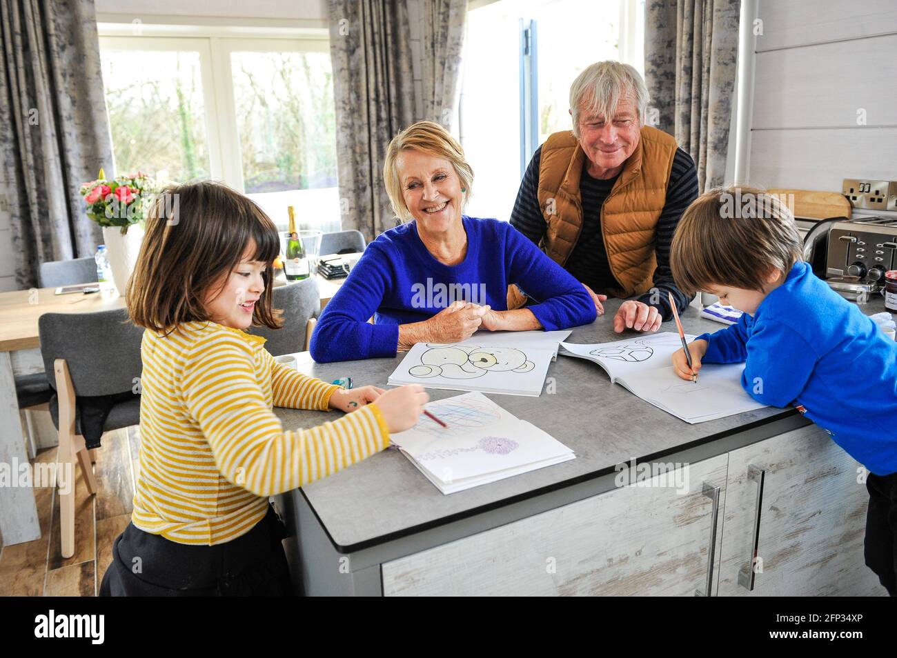 A retired couple spending time with their grandchildren on a holiday in Cornwall UK. Entertaining the grandchildren drawing and colouring pictures. Stock Photo