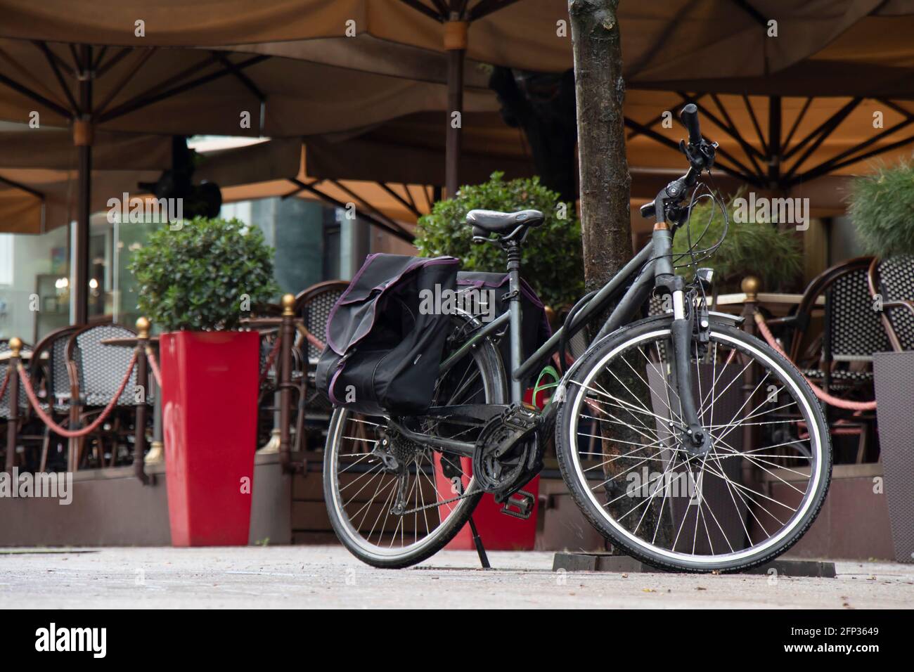 Black bicycle with double panniers bag parked under the tree by the cafe terrace Stock Photo