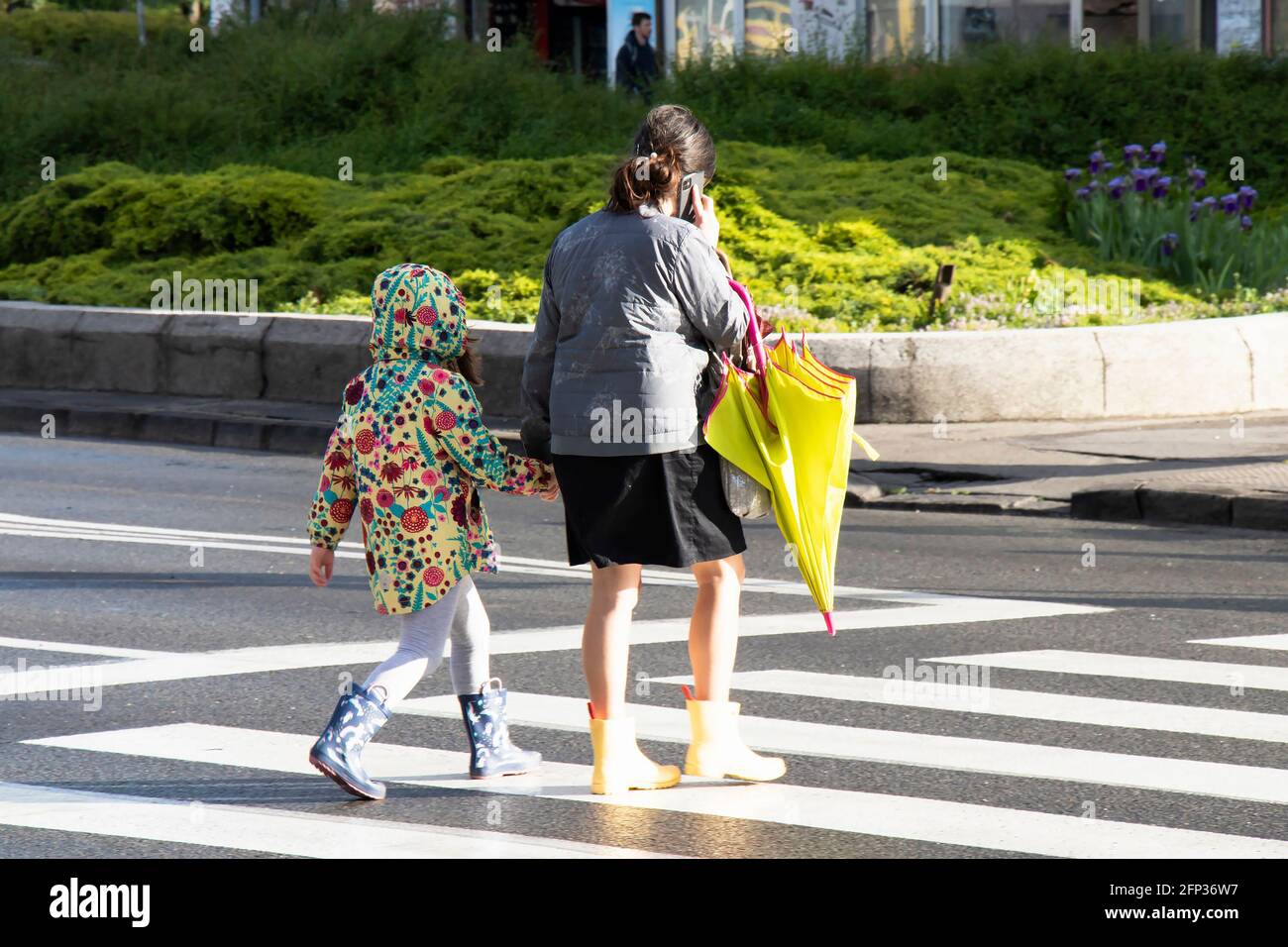 Belgrade, Serbia - May 13, 2021: Woman and a girl walking hand in hand while crossing the street on a bright sunny and rainy day Stock Photo