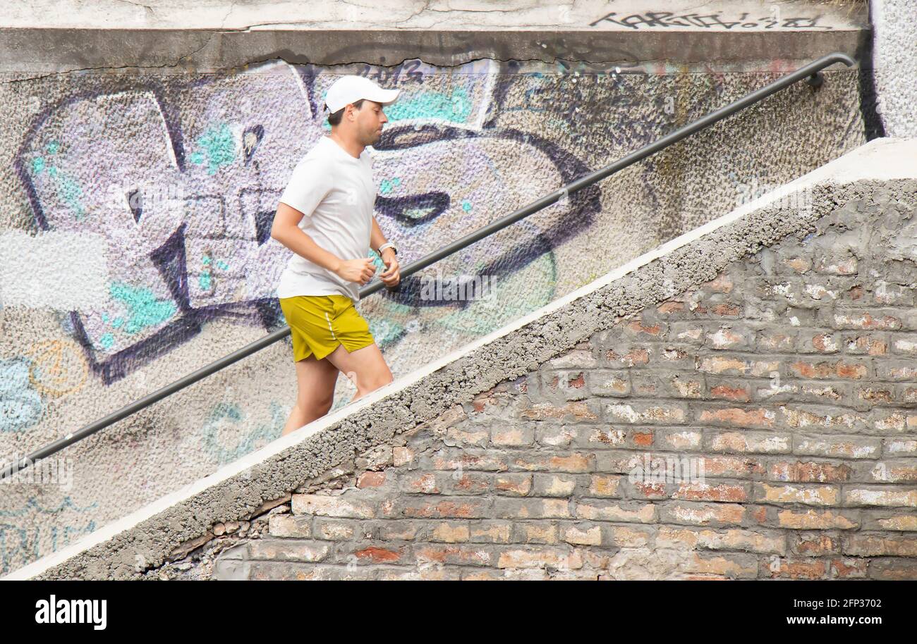 Belgrade, Serbia - May 14, 2021: One young man jogging alone and running up outdoor city stairs on a sunny day Stock Photo
