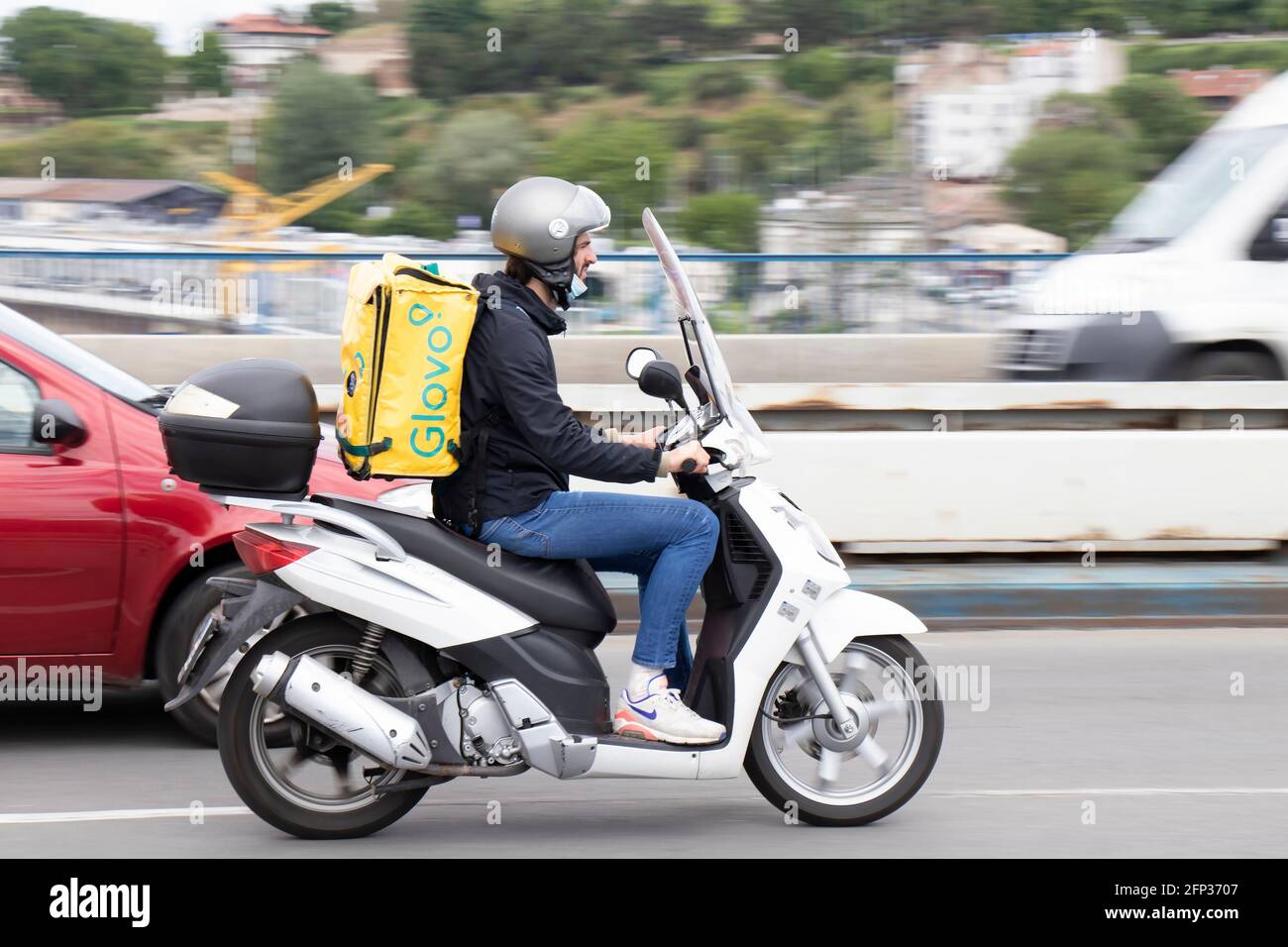Belgrade, Serbia - May 13, 2021: Courier working for Glovo food delivery service riding a scooter on city highway over the bridge Stock Photo