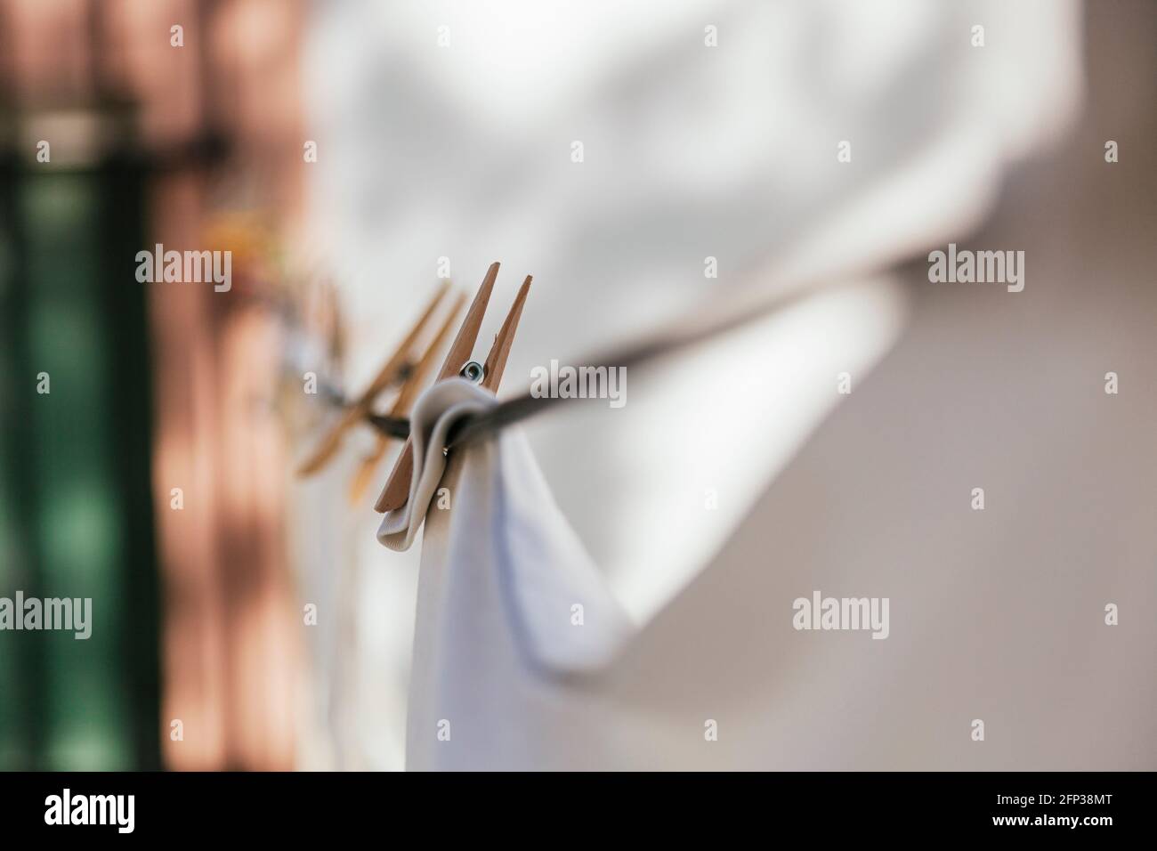 White clothes hanging on a clothesline with wooden clothespins. The clamp is in focus, the rest is out of focus. A window with black bars can be seen Stock Photo
