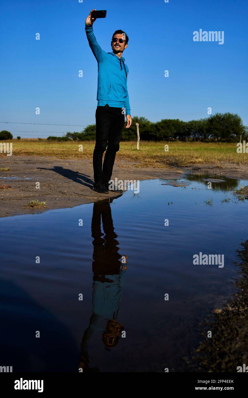 Young man smiling reflected in the water taking a selfie Stock Photo