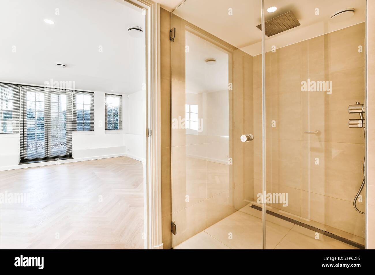 Beige tiled walls in bathroom with white double washbasin under mirror opposite to white tub