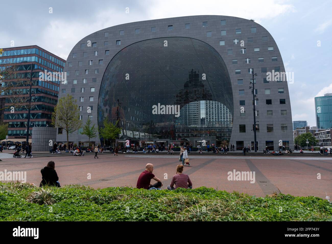 Rotterdam, Netherlands - 14 May, 2021: the Markthal building and train station with people relaxing and the city square in the foreground Stock Photo