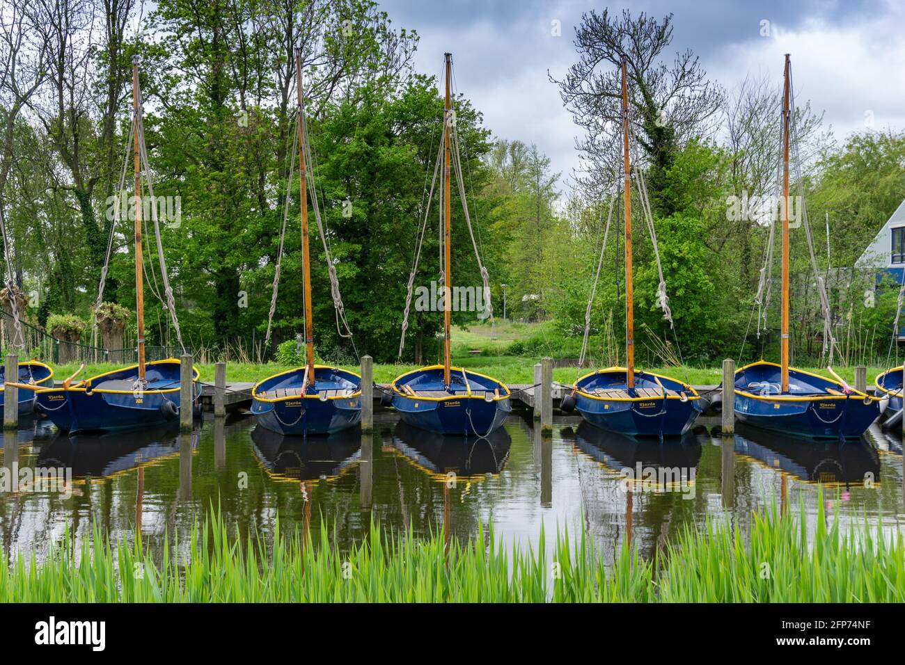 Sassenheim, Netherlands - 16 May, 2021: yellow and blue sailboats anchored in a row in a canal in southern Holland Stock Photo