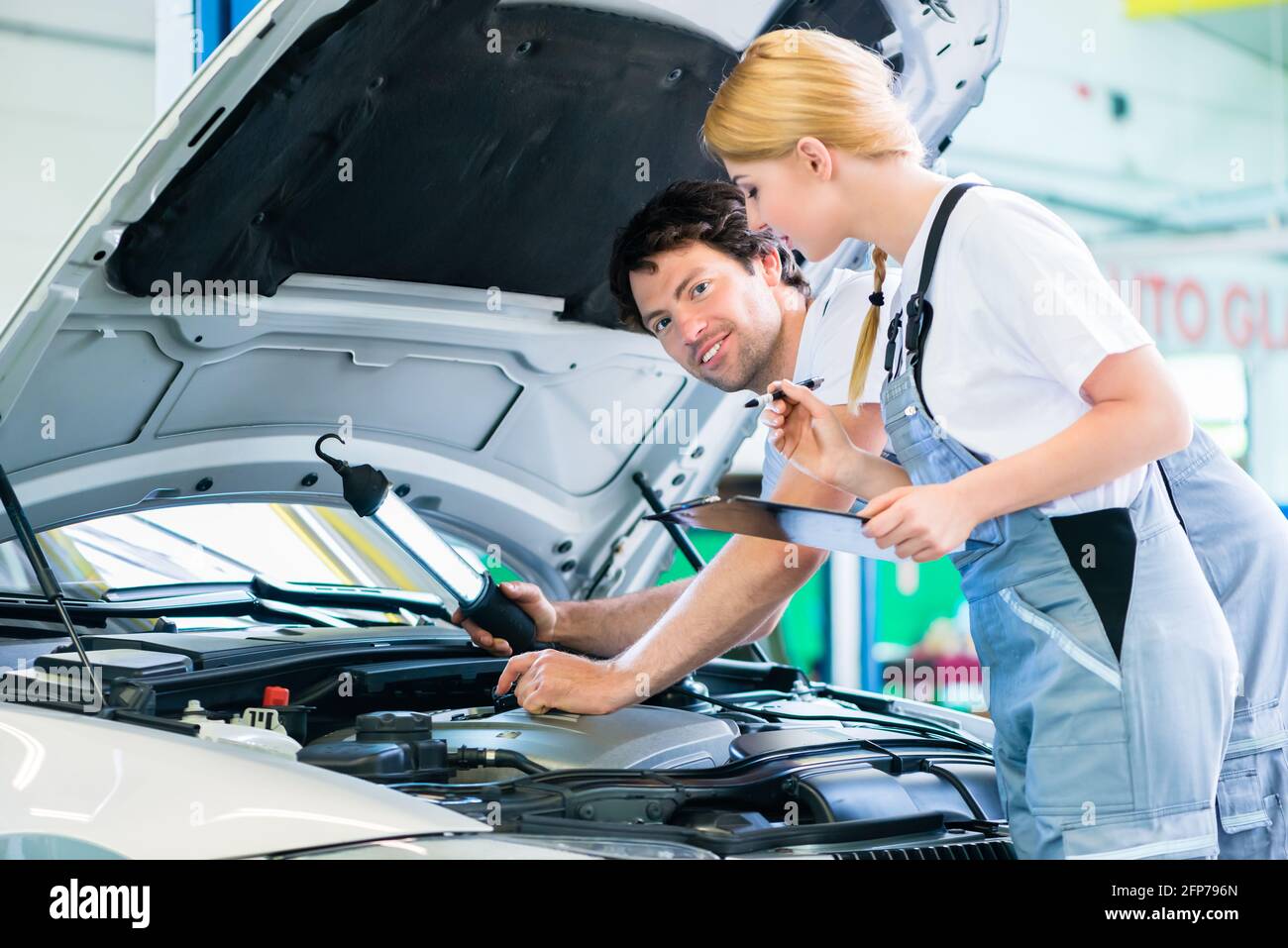 Male and female mechanic team examine car engine with light and ...