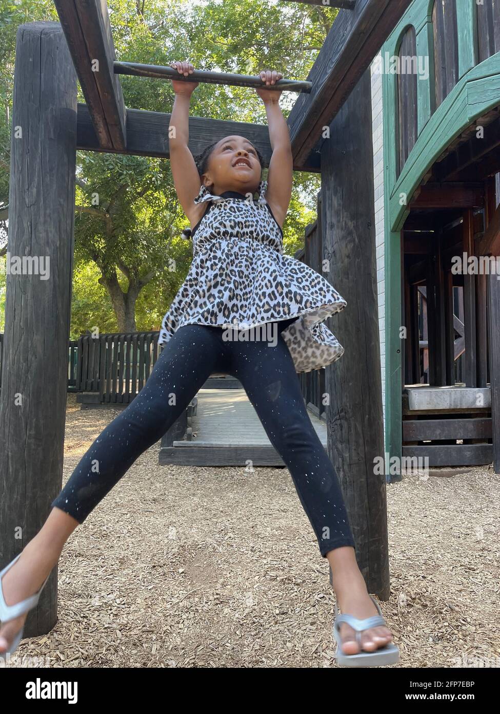 vertical shot of a young black girl swinging from monkey bars in a children's playground Stock Photo