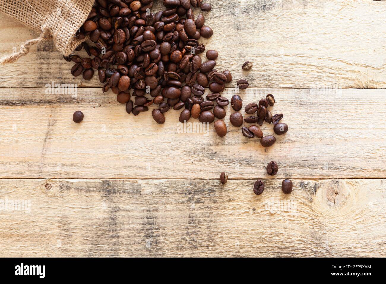 Small sack overturned on some pine wood boards where many roasted coffee beans are roasted. Stock Photo
