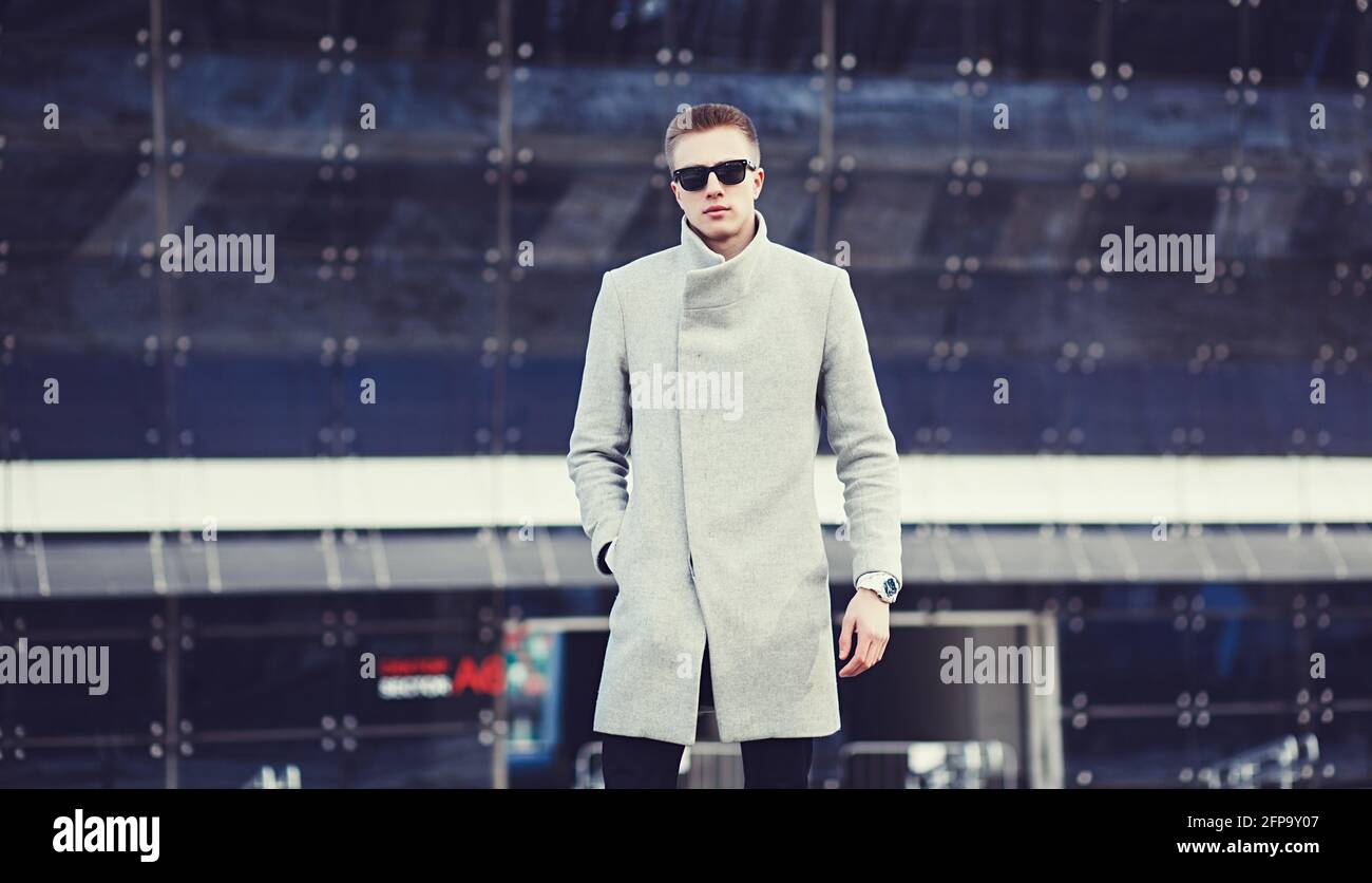 Stylish man wearing fashionable clothes, walking in the street. Young guy in coat with modern hairstyle in urban background Stock Photo