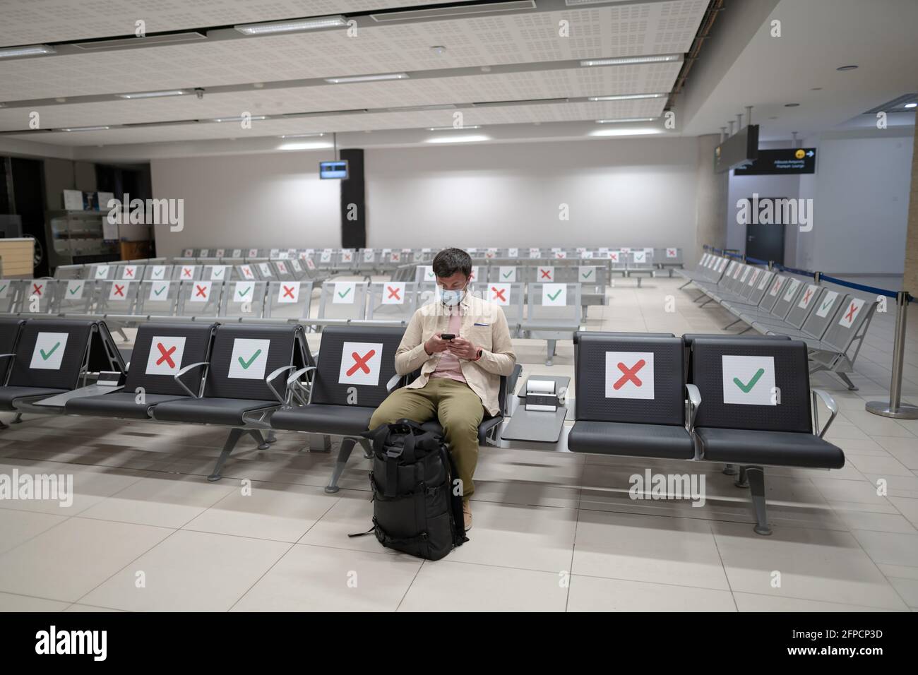 Waiting for flight at empty airport in Cyprus. Man sitting on chair with social distance marker at empty Paphos terminal. Flights canceled during Stock Photo
