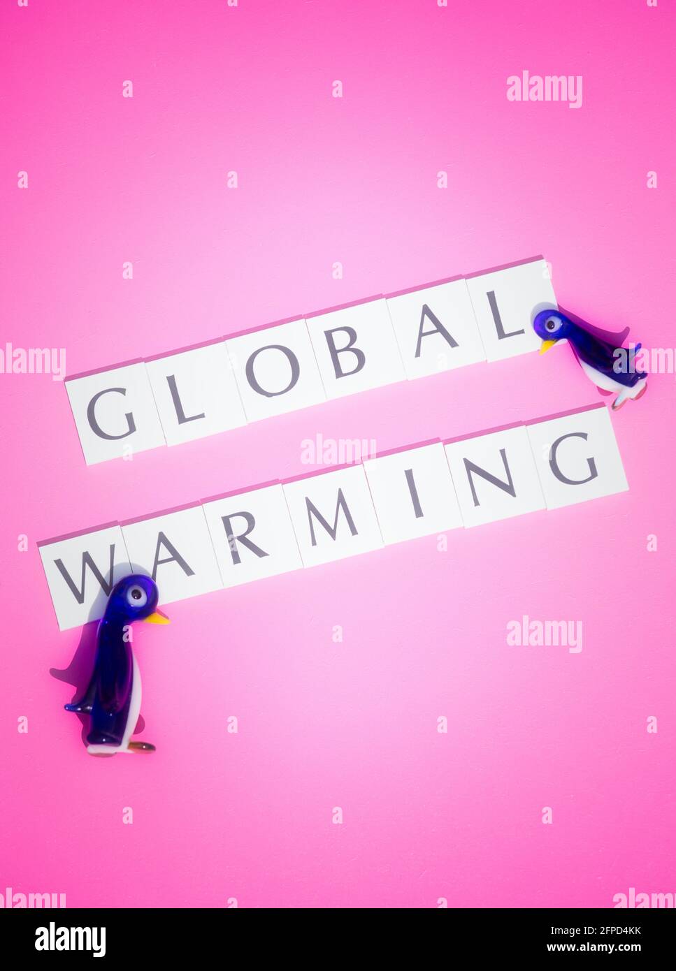 Directly above of two glass penguins and the words global warming on pink background. Concept of climate change, global warming, change Stock Photo