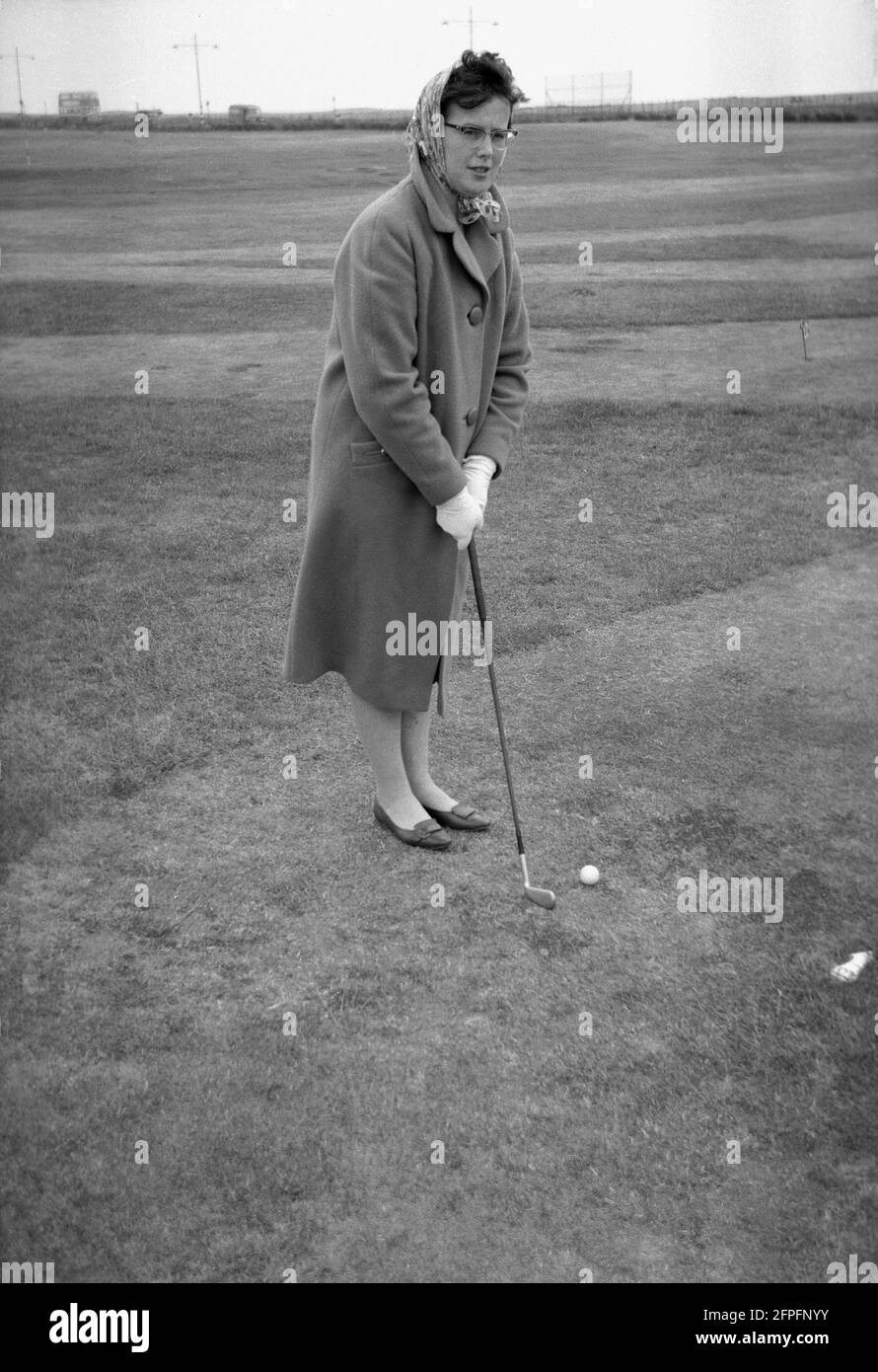 1962, historical, a lady in a long coat playing golf, on the seaside putting green or putting course, West Green, Littlehampton, West Sussex, England, UK. Stock Photo