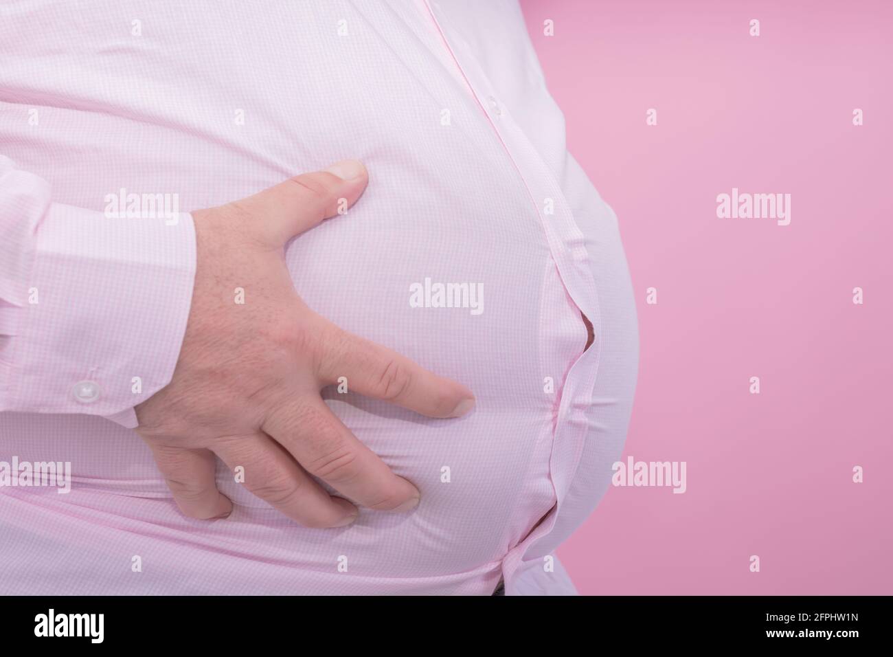 Fat man hand holding his big belly on a pink background typical photo