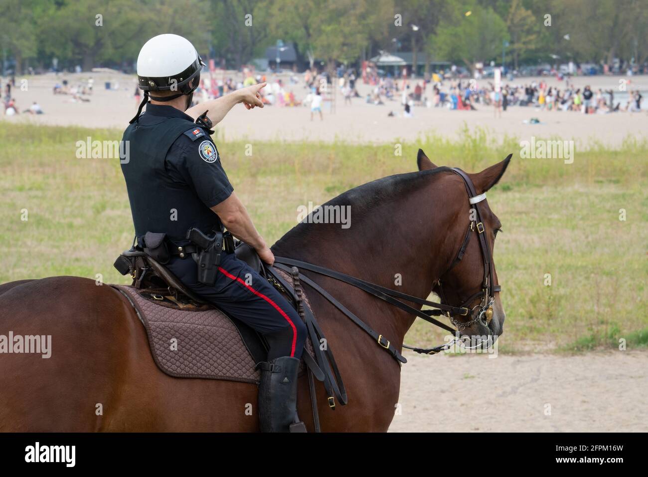 While the province was under a stay-at-home order due to COVID-19, a mounted police officer points at a crowded Woodbine Beach in Toronto, Ontario. Stock Photo