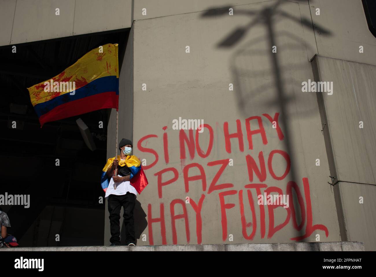 Bogota, Cundinamarca, Colombia. 19th May, 2021. Protester waves the Colombian flag while next to him there is a mural that says ''if there is no peace, there is no football'' against the realization of the American Cup in the country, while protests increase in BogotÃ¡ on May 20, 2021 in the context of a national strike in Colombia against the tax reform and the government of IvÃ¡n Duque. Credit: Daniel Romero/LongVisual/ZUMA Wire/Alamy Live News Stock Photo