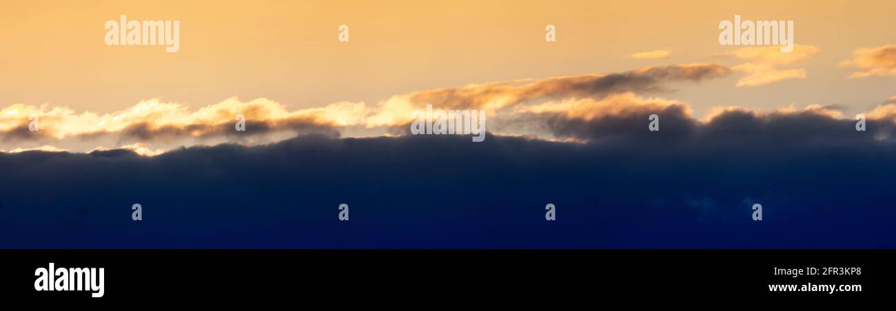 Evening sunset panorama with dark blue clouds and orange light clouds Stock Photo