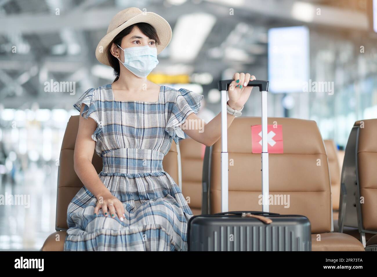 Young female wearing surgical face mask in airport terminal, protection Coronavirus disease (Covid-19) infection, Asian woman traveler sitting on chai Stock Photo