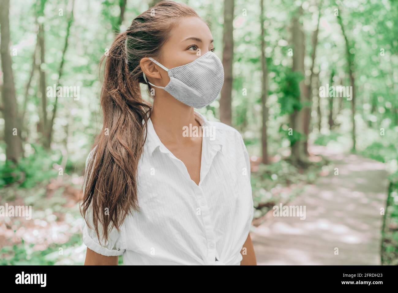Asian woman wearing fabric ppe face mask cover walking in summer forest woods nature. Coronavirus pandemic lifestyle. Eco-friendly environment concept Stock Photo