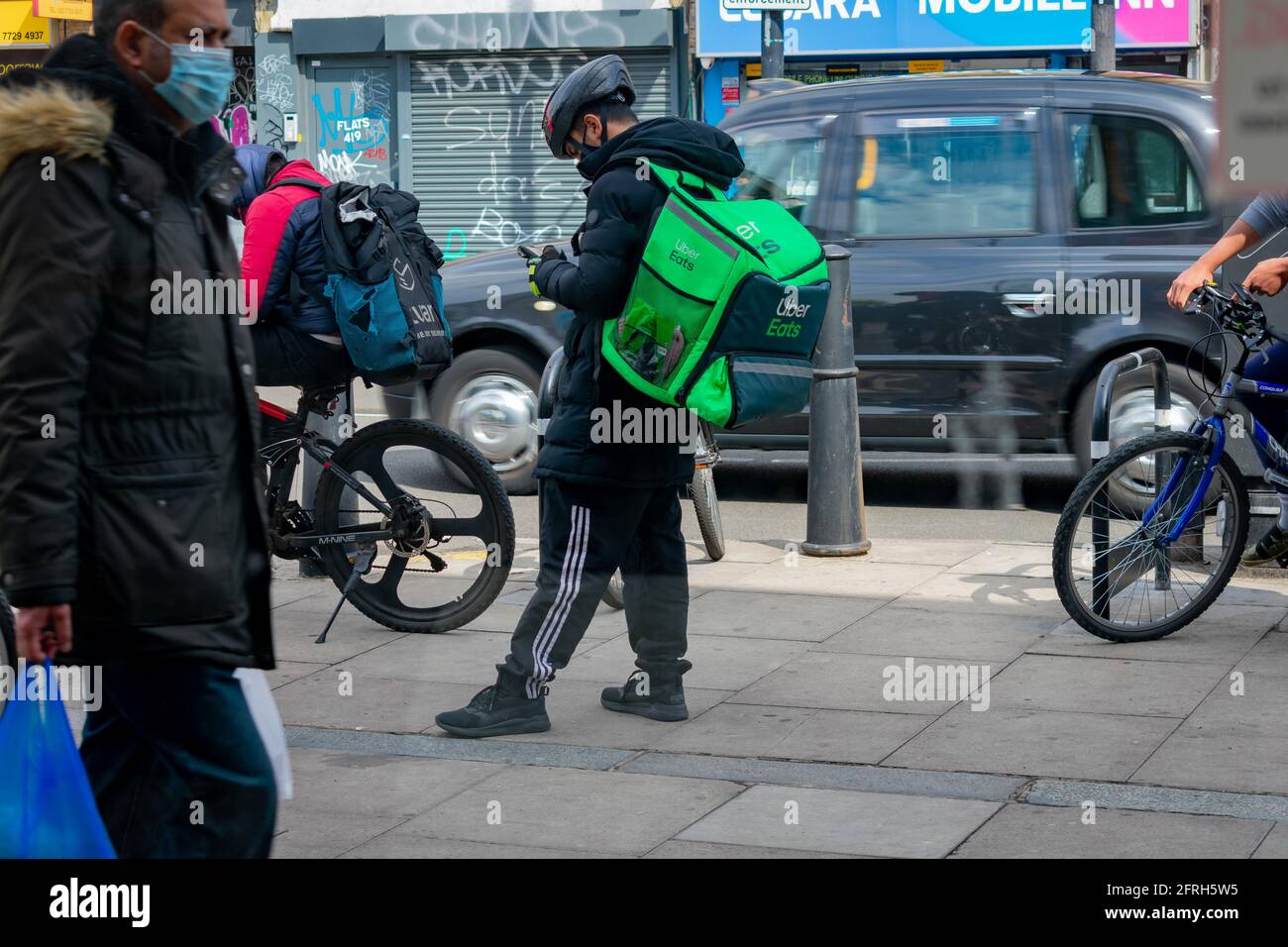 London. UK- 05.18.2021: young men working as self employed riders for online food ordering companies waiting for their next job notice on his phone. Stock Photo