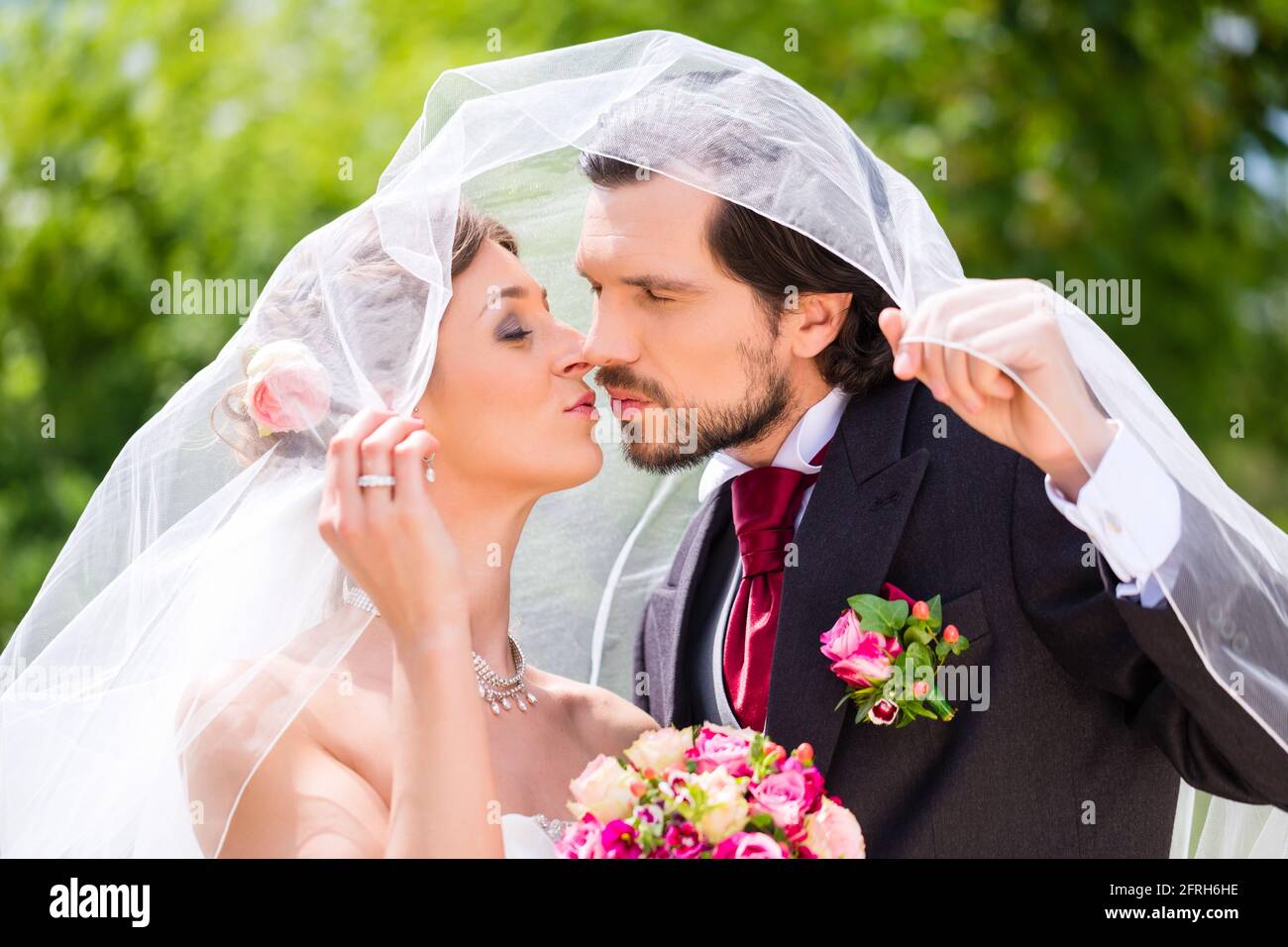 Bridal pair kissing under veil at wedding Stock Photo