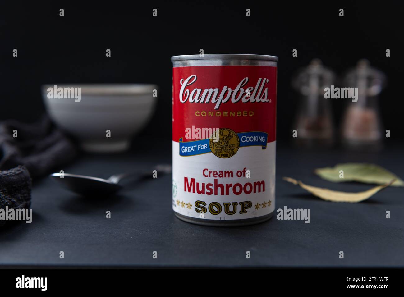 A tin of canned Campbell's cream of mushroom soup on a table with a dark background. Stock Photo