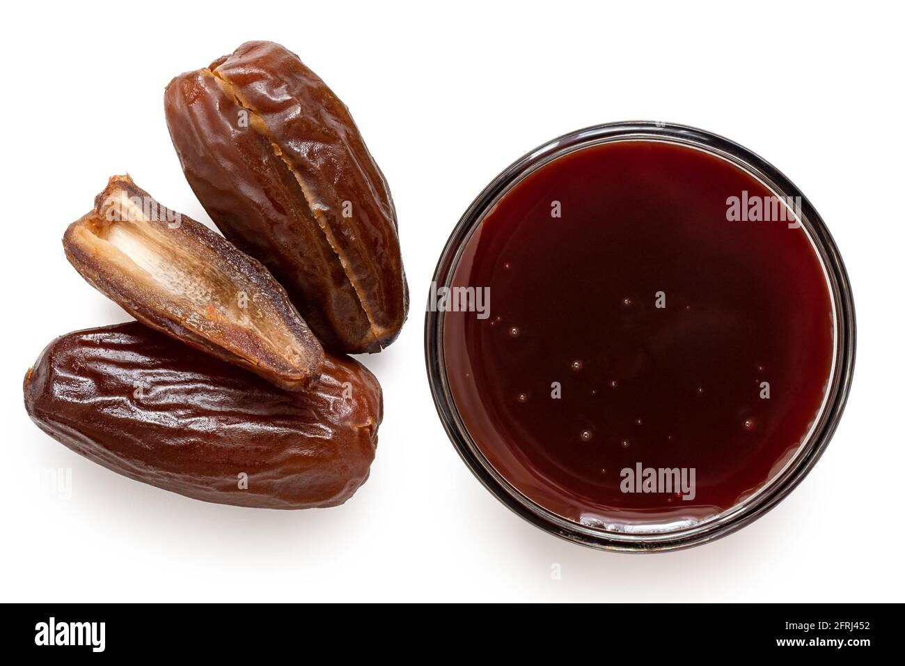 Date syrup in a glass bowl next to whole and cut dry pitted dates isolated on white. Top view. Stock Photo