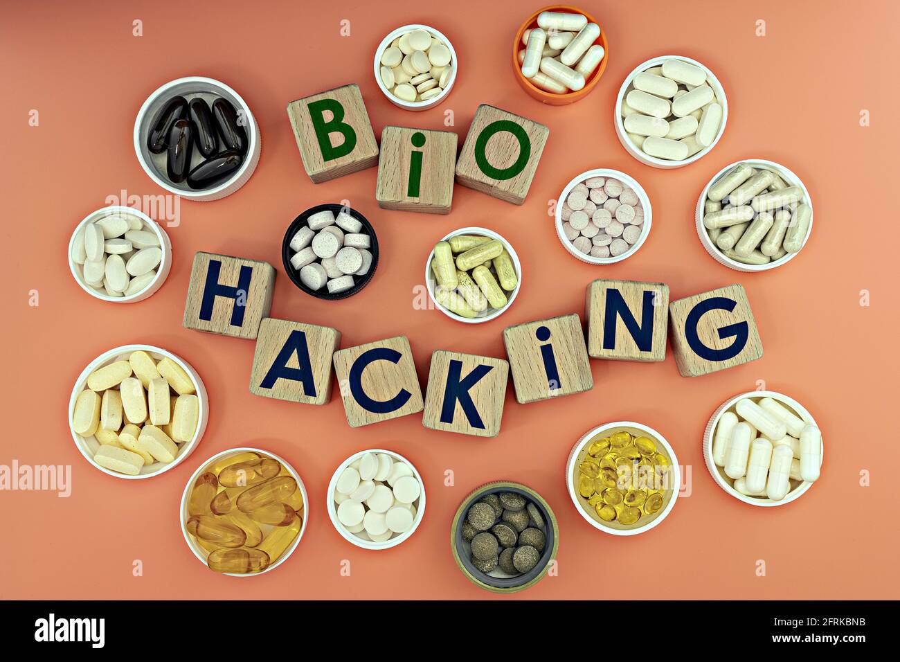 photo on biohacking theme. wooden cubes with the inscription 'biohacking', and biologically active supplements, on coral background Stock Photo