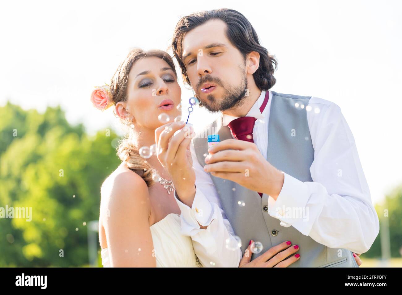 Wedding bride and groom blowing bubbles outside on field Stock Photo