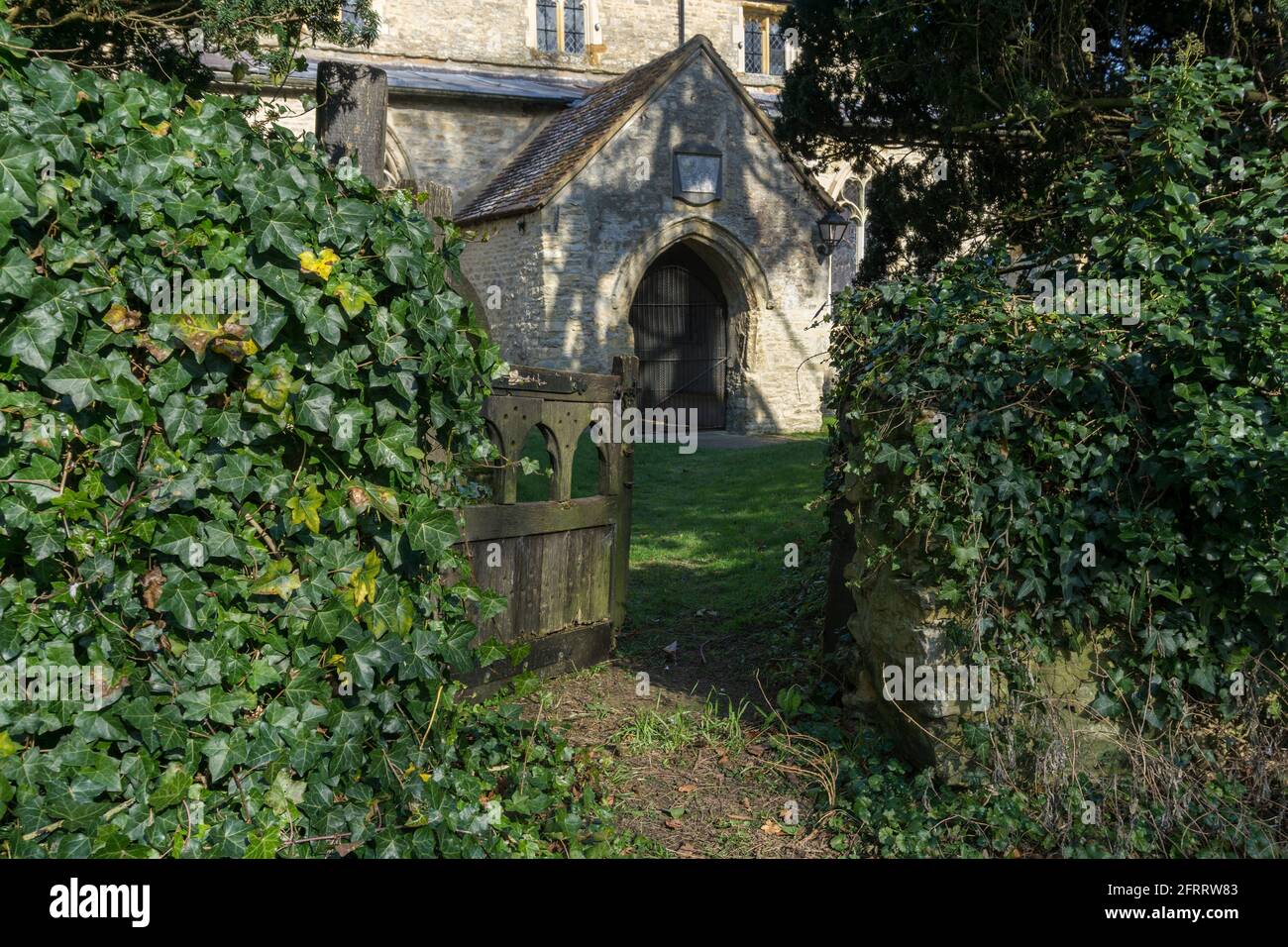 Old wooden gate in an overgrown ivy wall leading to the church of St Mary in the village of Haversham, Buckinghamshire, UK Stock Photo