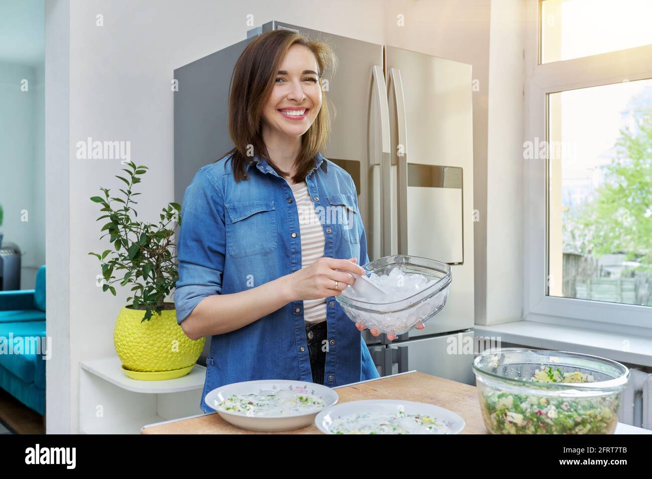 Smiling woman in kitchen near refrigerator with ice for cooling food Stock Photo