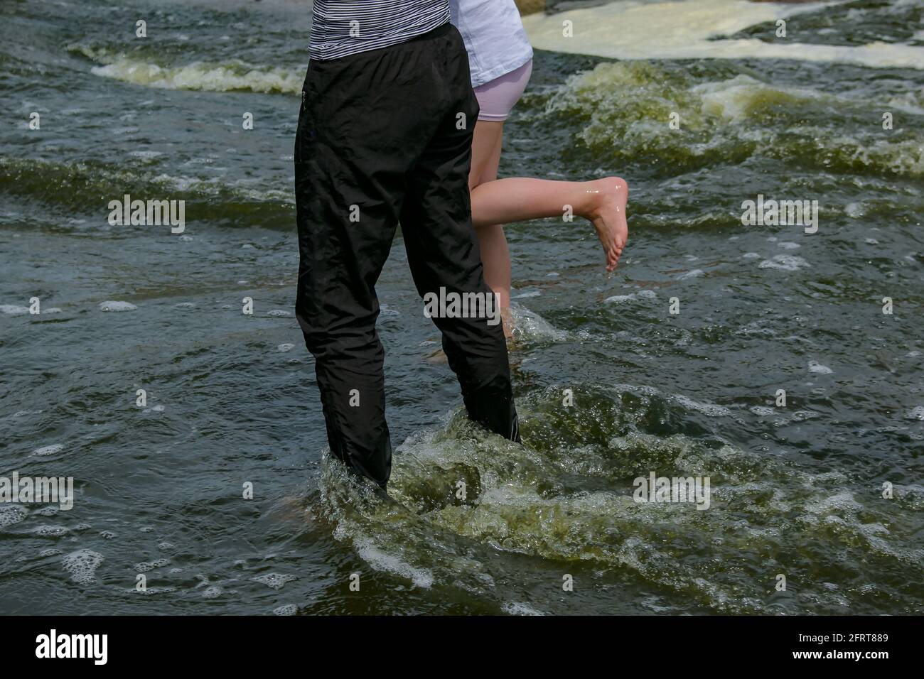 People are crossing the fast flowing river. Tourists walk over rocks in ...