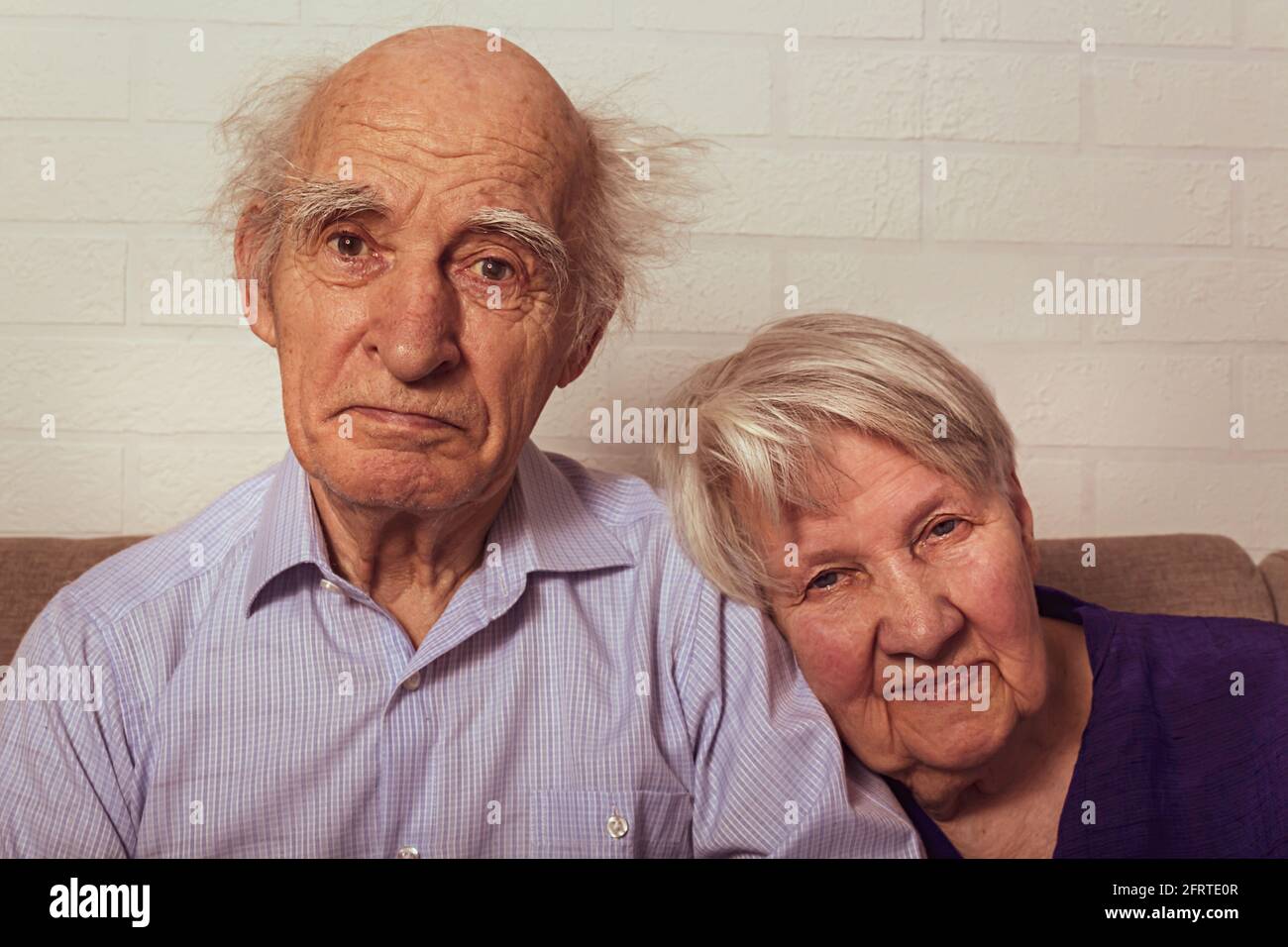 Very old grandma and grandpa cuddling on couch. Love in old age. Wife puts her head on husband's shoulder. Elderly people.  Stock Photo