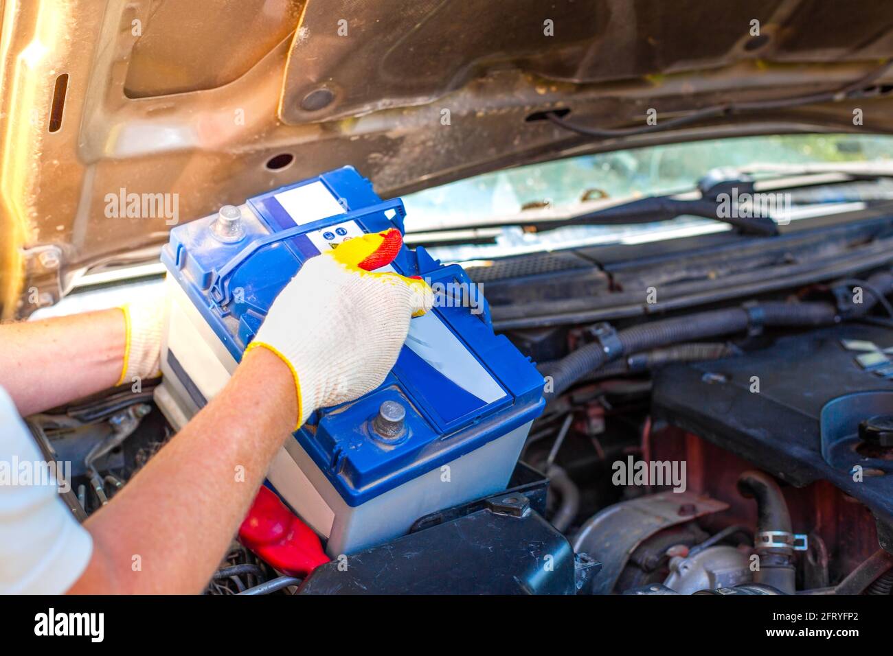 Maintenance of the machine. A male car mechanic takes out a battery from under the hood of a auto to repair, charge or replace it. Stock Photo