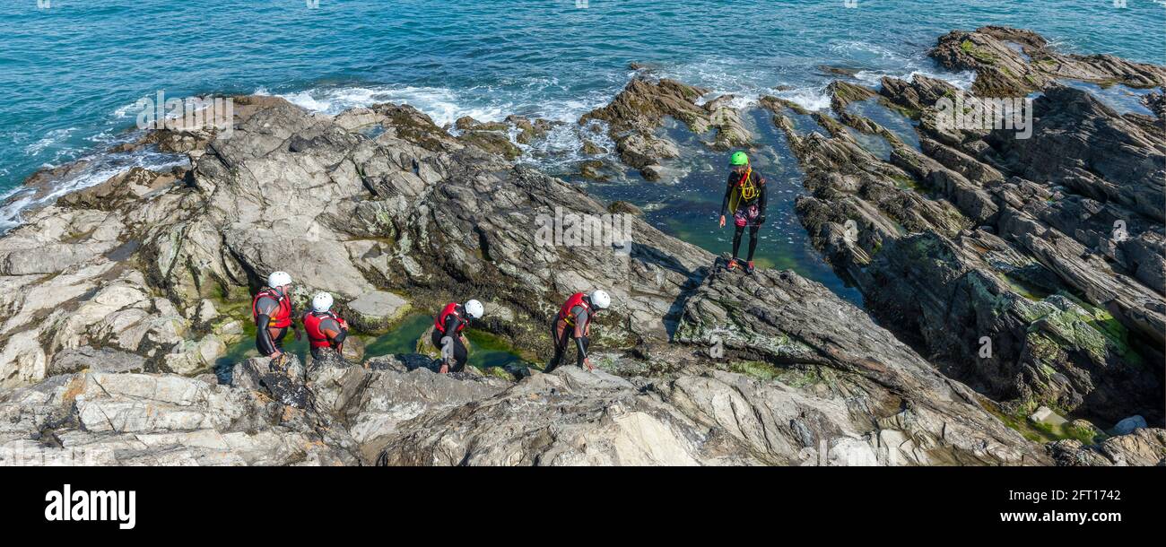 A panoramic image of holidaymakers and their guide walking across rocks on a coasteering adventure on Towan Head in Newquay in Cornwall. Stock Photo
