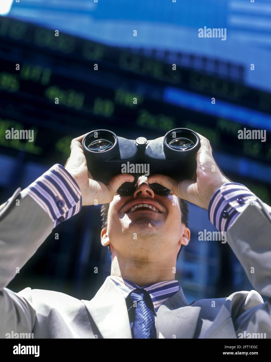2005 HISTORICAL SMILING OFFICE WORKER LOOKING UP THROUGH BINOCULARS (©STEINER-OPTIC GMBH 2000) BELOW ELECTRONIC STOCK MARKET PRICE TICKER DISPLAY Stock Photo
