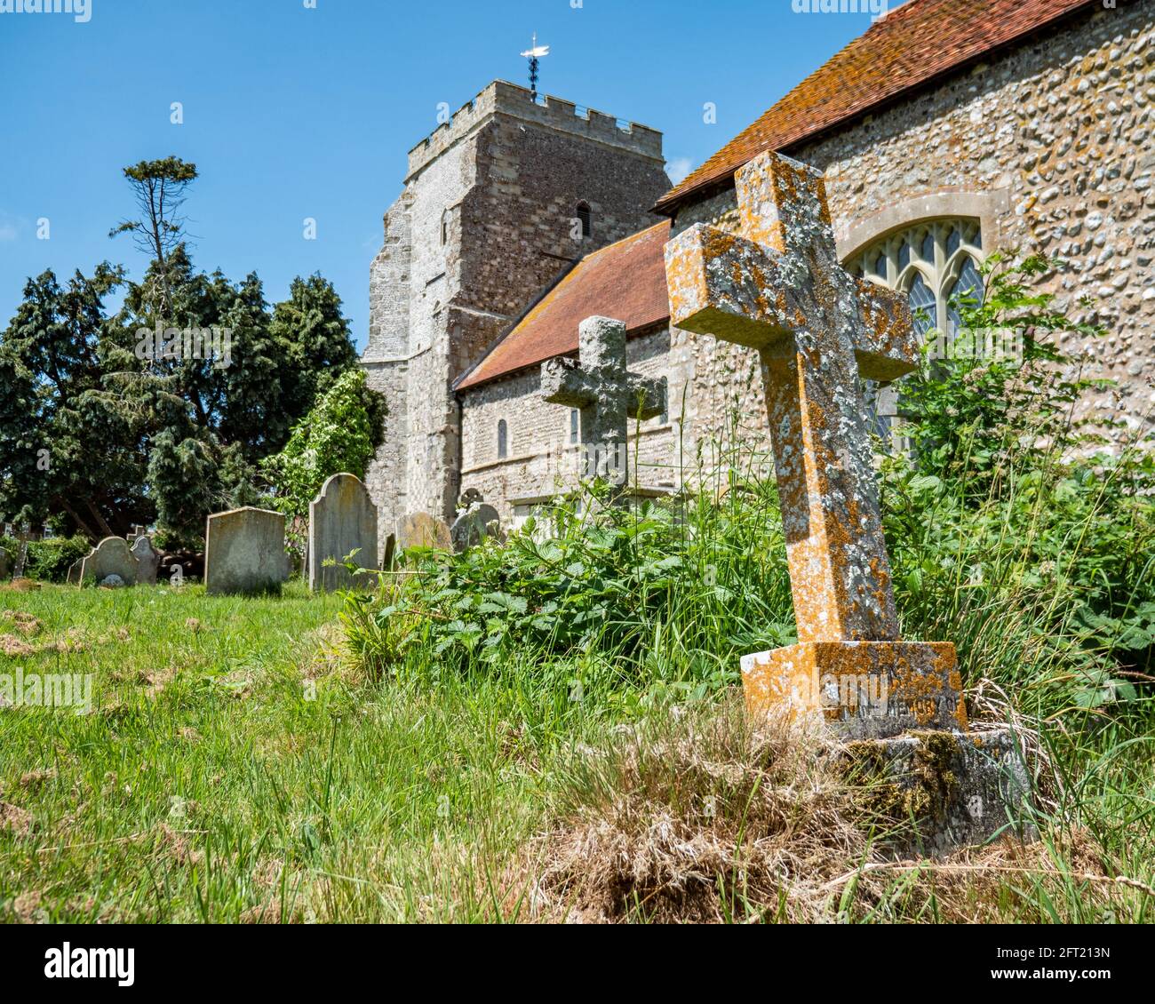 English Church Yard. A view of a typical English church and overgrown cemetery with the foreground dominated by a long forgotten crucifix grave stone. Stock Photo