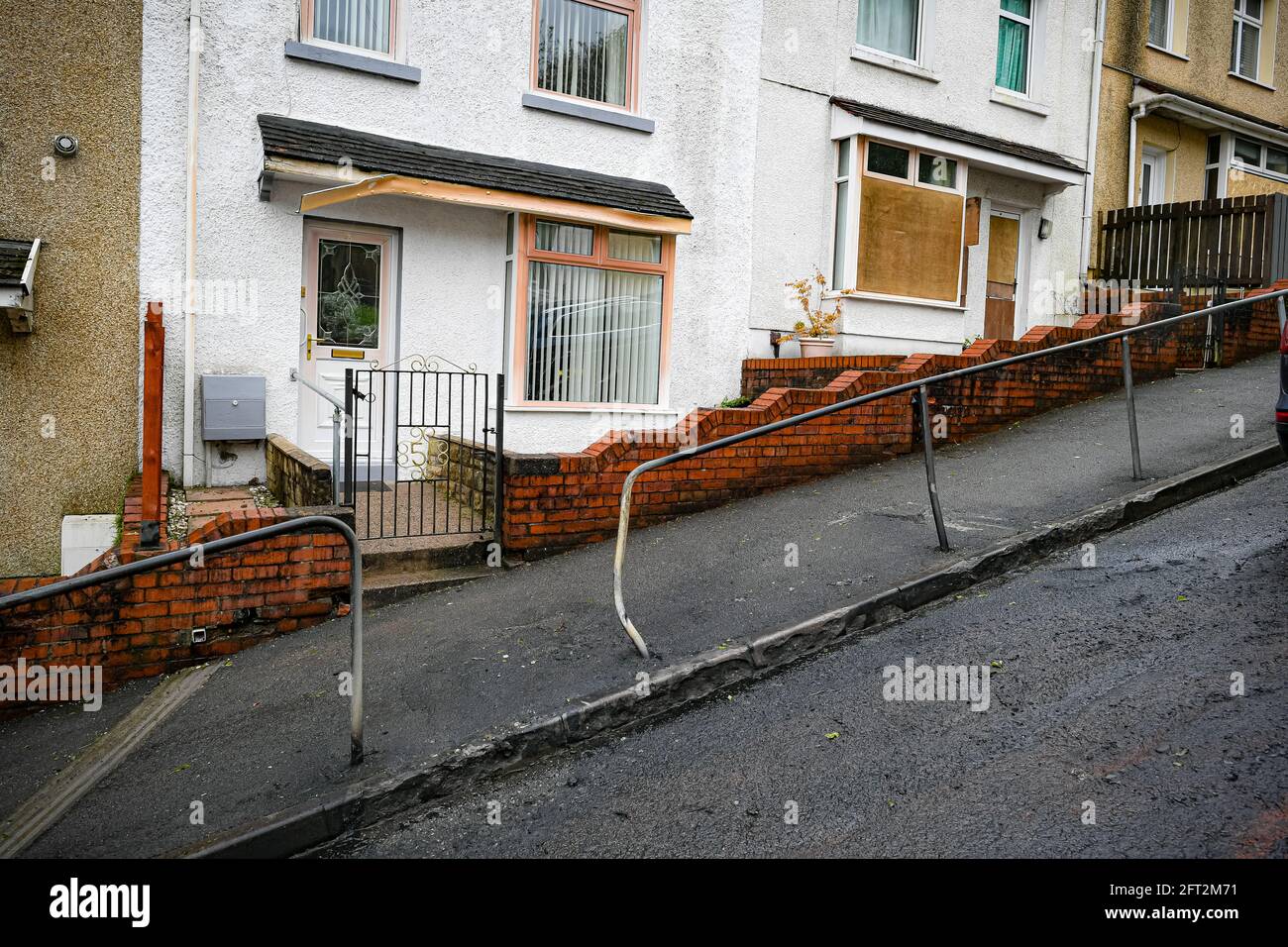 Blackened tarmac, damaged railings and boarded up houses at the top of