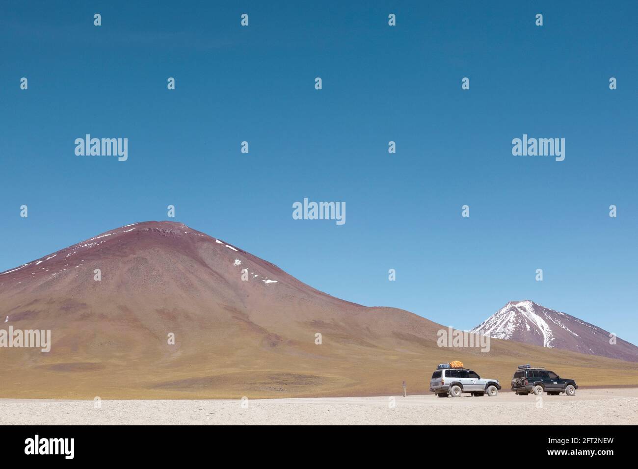 4x4 SUV over-land safari vehicles are seen at the edge of the Laguna Verde in the Bolivian desert. Stock Photo