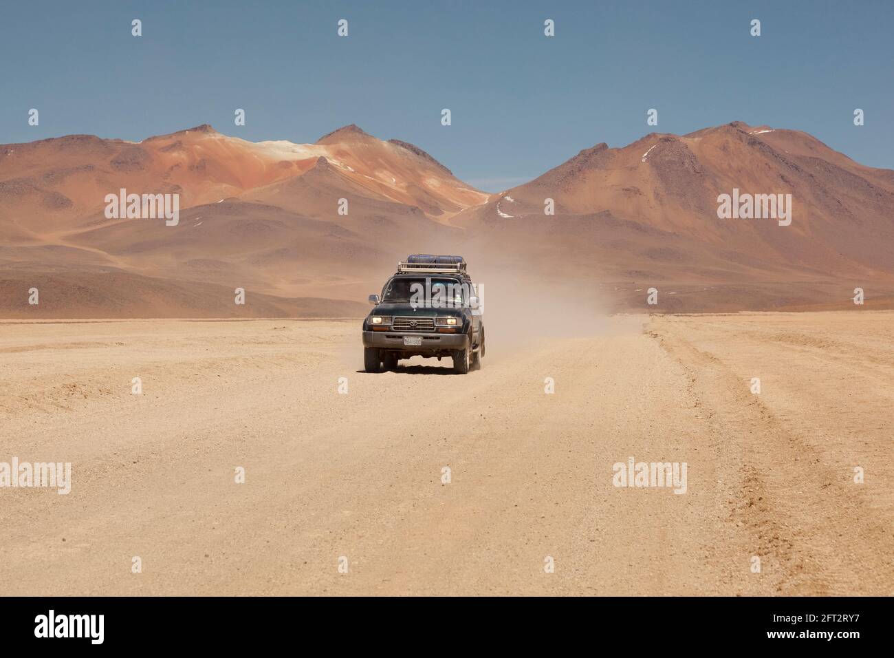Against a backdrop of volcanoes, a 4x4 off-road vehicle speeds across Bolivia's desert landscape on an overland tourist safari. Stock Photo