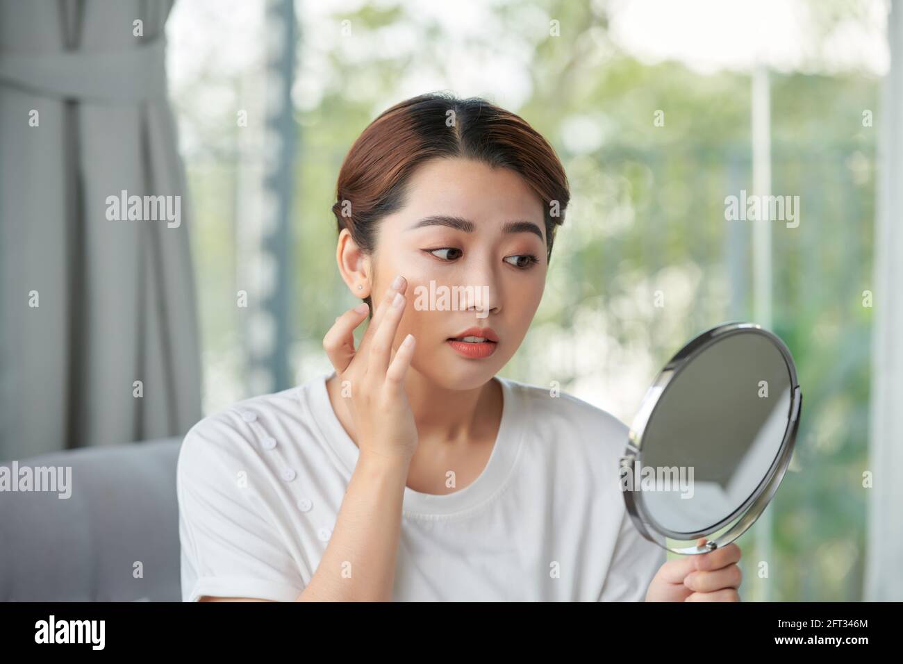 Woman examining her face in the mirror, problematic acne-prone skin concept Stock Photo