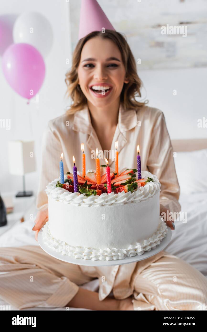 Birthday cake with candles in hands of blurred woman on bed Stock Photo ...